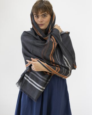 Image: Model wearing large wool scarf in charcoal grey with silver and orange silk stripe